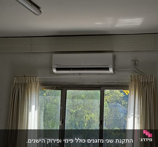 מזגן מותקן מעל חלון עם וילונות לבנים